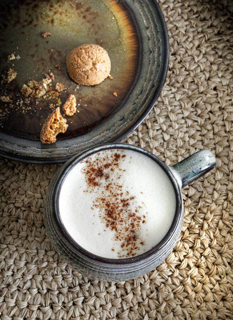 Keramische koffiemok met latte en koekjes op een rustieke ondergrond.