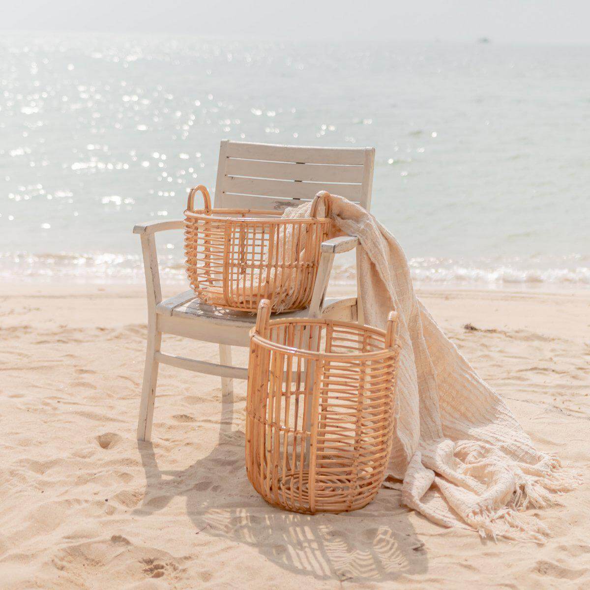 Opbergmand JEMUH van rotan op strand met stoel en deken, perfect als wasmand, duurzaam en handgemaakt, twee maten beschikbaar.