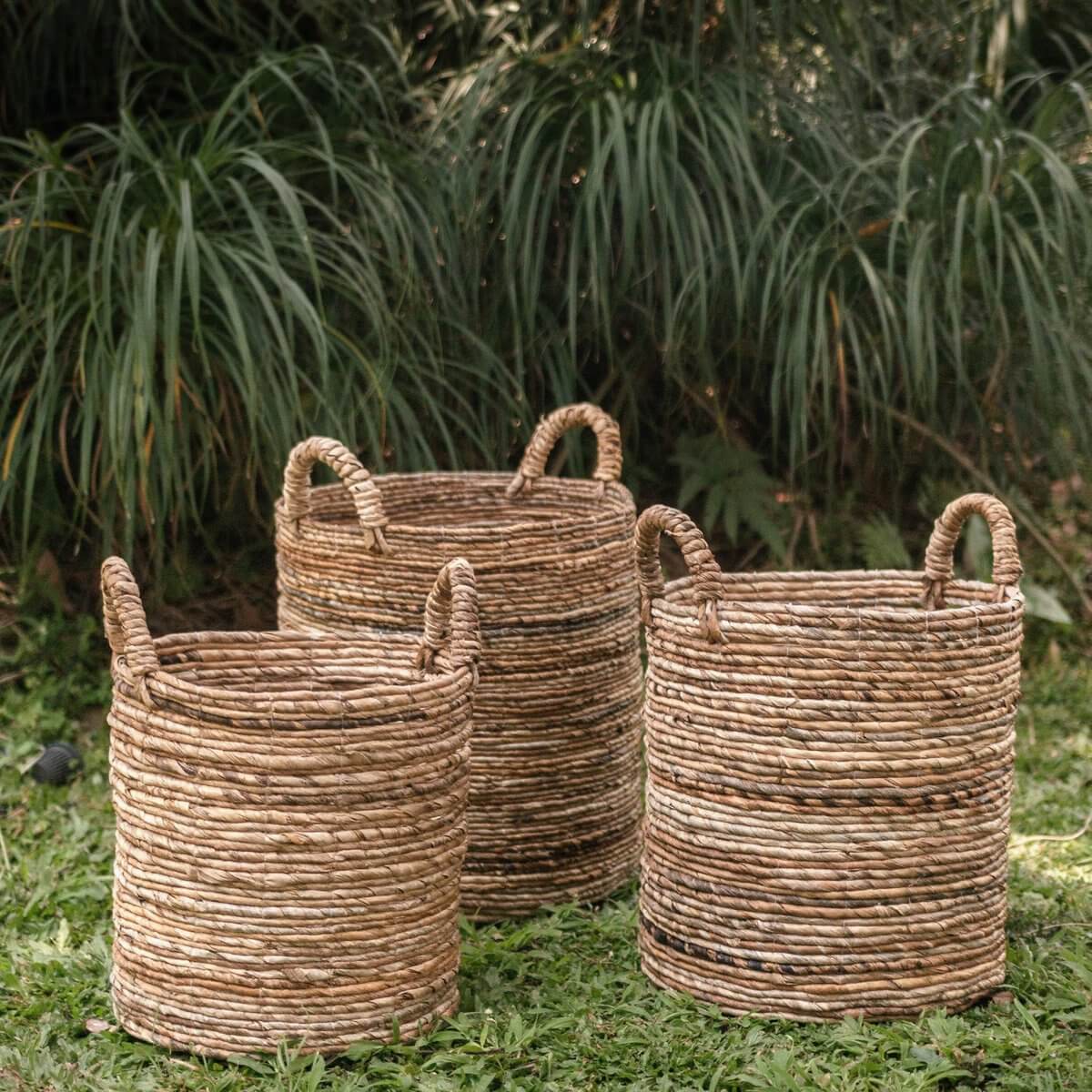 Drie opbergmanden van bananenvezel met handvatten op gras, ideaal als wasmand of plantenbak, handgemaakt en duurzaam zonder plastic. Nederlands talig.