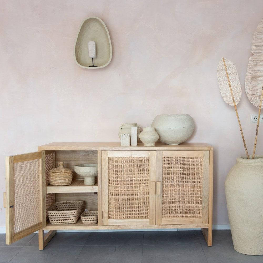 Houten dressoir met rieten deuren en vaas, decoratieve items en natuurlijke charme in een stijlvolle woonkamer.