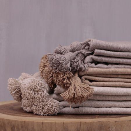 Stapel van beige pompom dekens op houten tafel, perfect voor een modern of boho interieur en gezellige avonden thuis.