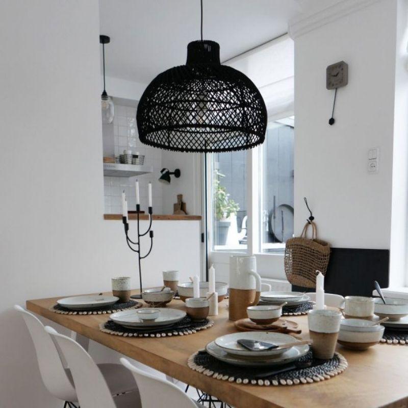 Rotan hanglamp Debby in landelijke eetkamer, perfect voor sfeervol dineren. Elegante zwarte lamp boven houten tafel met servies.