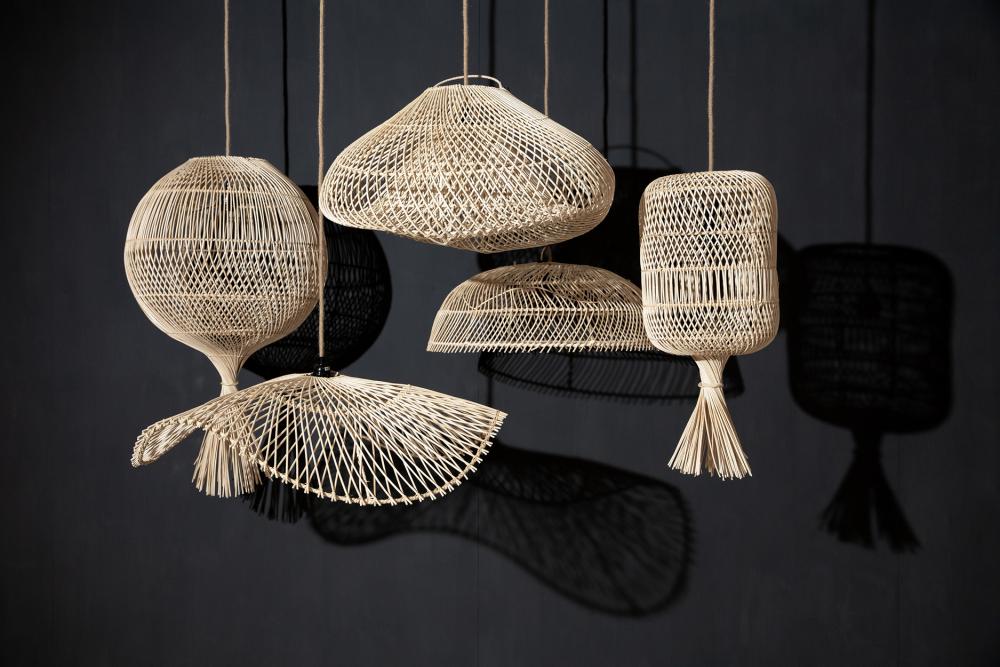 Een verzameling van handgemaakte rotan hanglampen in verschillende vormen, boho chic stijl, hangend tegen een donkere achtergrond.